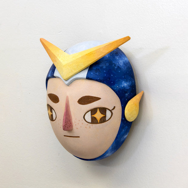 Sculpture of a person's head with a solemn yet sweet expression. They wear a helmet like a superhero with blue stripes and a large yellow arrow.