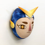 Sculpture of a person's head with a solemn yet sweet expression. They wear a helmet like a superhero with blue stripes and a large yellow arrow.