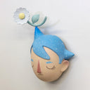 Sculpture of a person's head with a solemn yet sweet expression. They have pointed blue starry hair with a white flower sitting atop their head.