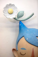 Sculpture of a person's head with a solemn yet sweet expression. They have pointed blue starry hair with a white flower sitting atop their head.