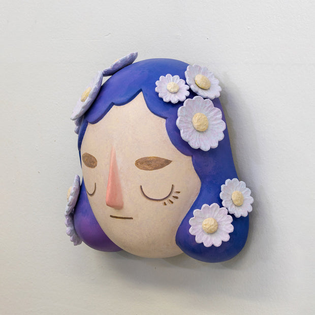 Sculpture of a person's head with a solemn yet sweet expression. They have mid length purple hair with white flowers all over like hair pins.