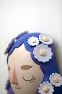 Sculpture of a person's head with a solemn yet sweet expression. They have mid length purple hair with white flowers all over like hair pins.