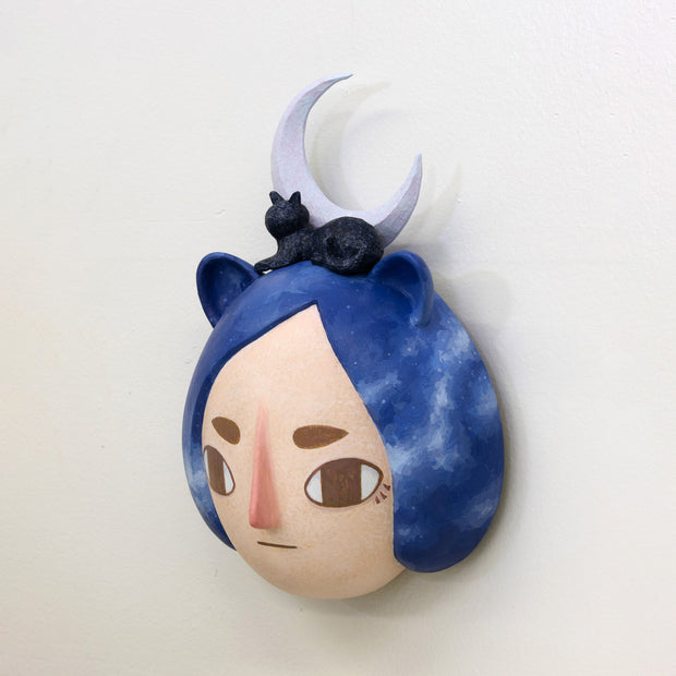 Sculpture of a person's head with a solemn yet sweet expression. They have mid length blue galactic pattern hair and small animal ears. A cat and a purple crescent moon sit atop their head.