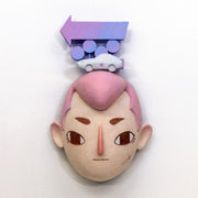 Sculpture of a person's head with a solemn yet sweet expression. They have pink hair and atop their head sits a white muscle car and painted signage.