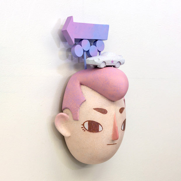 Sculpture of a person's head with a solemn yet sweet expression. They have pink hair and atop their head sits a white muscle car and painted signage.