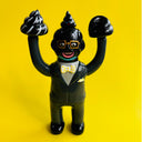 Vinyl figure of a Satoshi Yamamoto, a Japanese business man, painted in a black and grey color scheme including his skin, with a piece of poo on his head and on both of his lifted up hands.