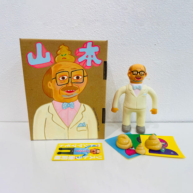 Soft vinyl figure of a man with glasses, wearing a pastel yellow suit and blue bowtie. Near his feet are 3 yellow poop swirls. It stands next to a painted box.