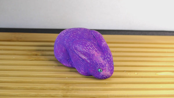 Video of water being poured over a purple sculpture of a sitting bunny, which then turns bright pink.