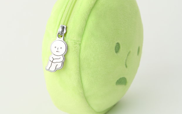 Close up of silver zipper accessory on a round plush pouch shaped like Smiski's head. The zipper is of Smiski sitting with their knees pulled into their chest.