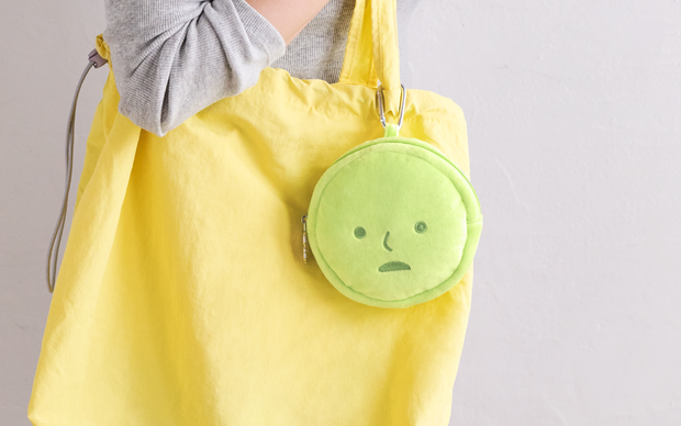 A green, circular plush pouch shaped like Smiski's head attached to a yellow tote bag.