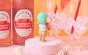 Fentimans Raspberry Lemonade bottles with a small figurine and glasses on a colorful background