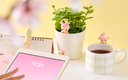 Table with tablet, mug of tea, and small plant with decorative figures on a yellow background