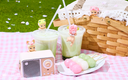 Picnic setting with a woven picnic basket, dango, matcha drinks and a small radio with Cherry Blossom Sonny Angel Hippers around.