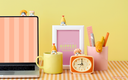 Colorful desk setup with laptop, mug, clock, and stationery on a checkered tablecloth.