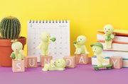 6 mini figures of Smiski characters, in various poses related to relaxation or fun activities. Options are: watering plant, blowing bubbles, sleeping w/ cat, flying a paper plane, skateboarding and playing ukelele.
