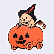 Die cut sticker of a ghost wearing a witch's hat and riding in a jack o lantern like its a car.