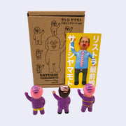 Set of 3 small vinyl figures of little business men. One wears a purple suit and waves. Another has pink hair, purple skin and wears a yellow briefs. The final figure has pink hair, purple skin and wears yellow bondage type attire. Back view.