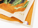 Close-up of a decorative tea towel with floral patterns and a brand label on a white background