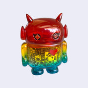 Rainbow colored soft vinyl figure with a black line art drawing inside its body, with mechanical imagery. Figure is shaped like a smaller Big Boss Robot, with a bigger head than normal and two black eyes with sparkles as pupils. A red heart is on its upper right chest.