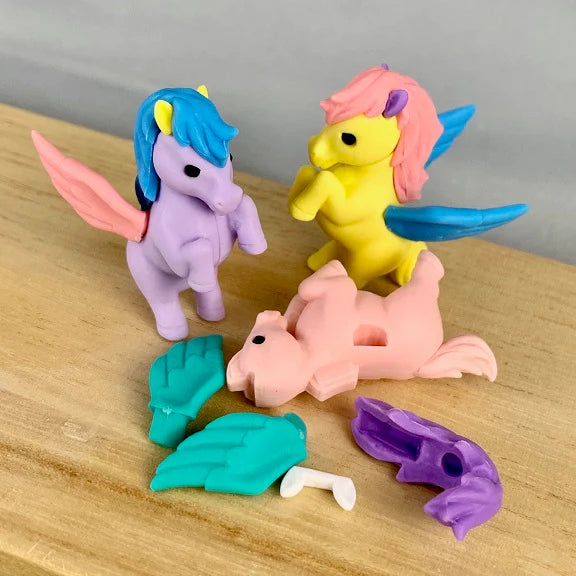 Colorful erasers shaped to look like unicorns, some with pegasus wings. One is disassembled with its wings, mane and ears separated into individual erasers.