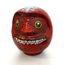 Daruma doll painted over in red paint with white monster teeth and yellow teeth.