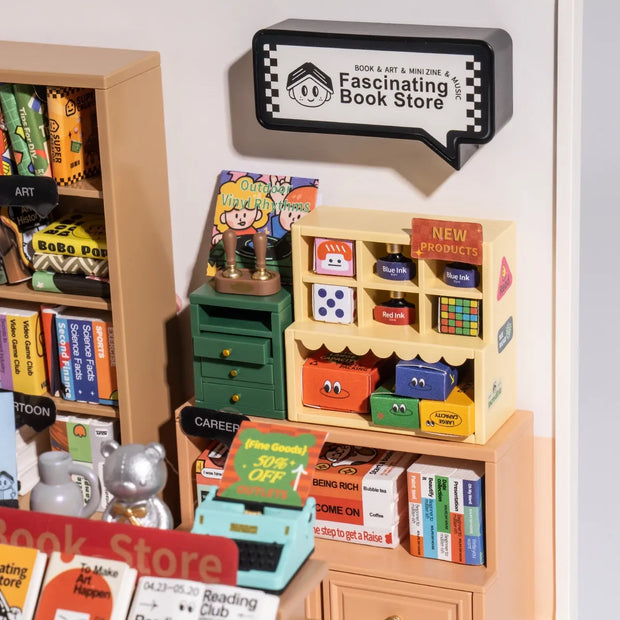 Detail shot of a diorama of a bookstore, with a sign that reads "Fascinating Book Store" above a series of shelves that hold books and various stationery items. 