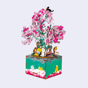 Fully assembled 3D kit of a music box, made out of small wooden pieces with cats sitting at the base of a blooming cherry blossom tree.