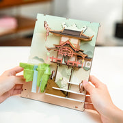 Partly assembled 3D bookend, with a pagoda style building as well as green hills and a waterfall nearby.