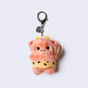Plush keychain of a fluffy pinkish orange monster with tiny yellow horns and tiny fangs. It wears a cheetah skin loin cloth and holds a spiked club.