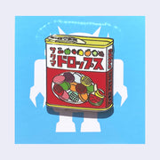 Die cut enamel pin of a tin of candy, Sakuma Drops, red and white packaging with drawings of fruit all over it. There is Japanese kanji written along the top and side of the container. On blue backing card.