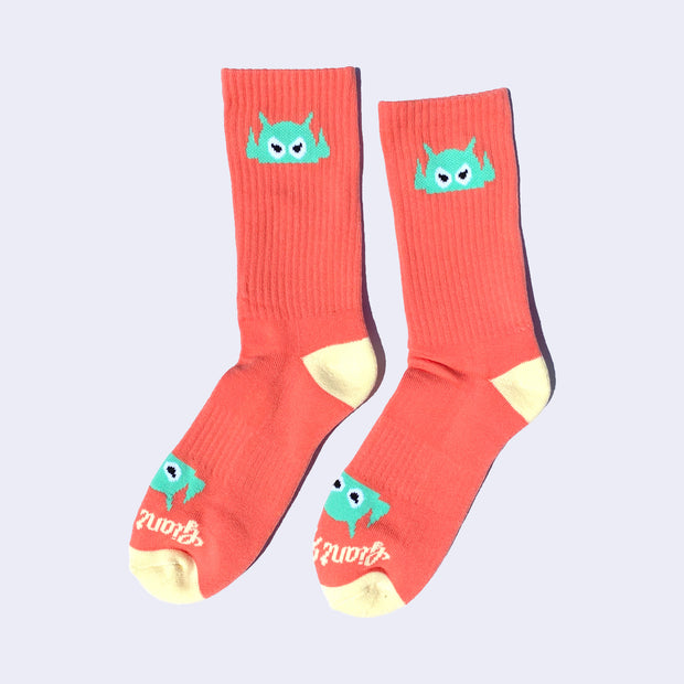 Salmon pink socks with a mint green cartoon robot head on them and cream colored heels and toes. The robot head decorates the cuff end of each sock so that it peeks out when you wear sneakers.
