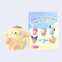 Small, flocked figurine of Pompompurin in a fuzzy costume holding a fuzzy orange bone. He sits next to the blind box packaging.