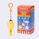 Blind box with Sanrio Characters on it and fireworks in the background. Next to it is a keychain of Pompompurin as a whistle.