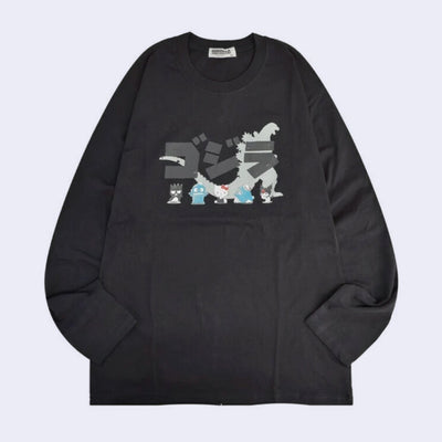 Dark gray long sleeve shirt with a silhouette of Godzilla with Japanese kanji atop of it. In front of Godzilla stand 5 Sanrio characters, very small in comparison: Badtz-Maru, Hangyodon, Hello Kitty, Tuxedo Sam and Kuromi.