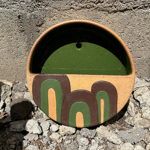 Ceramic circular vessel, terracotta color with brown and green curved lines, abstract and geometric. Interior of vessel is olive green.