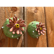 Ceramic sculpture of a pair of peyote cacti, with small white spikes and large blossomed pink flowers in the center.