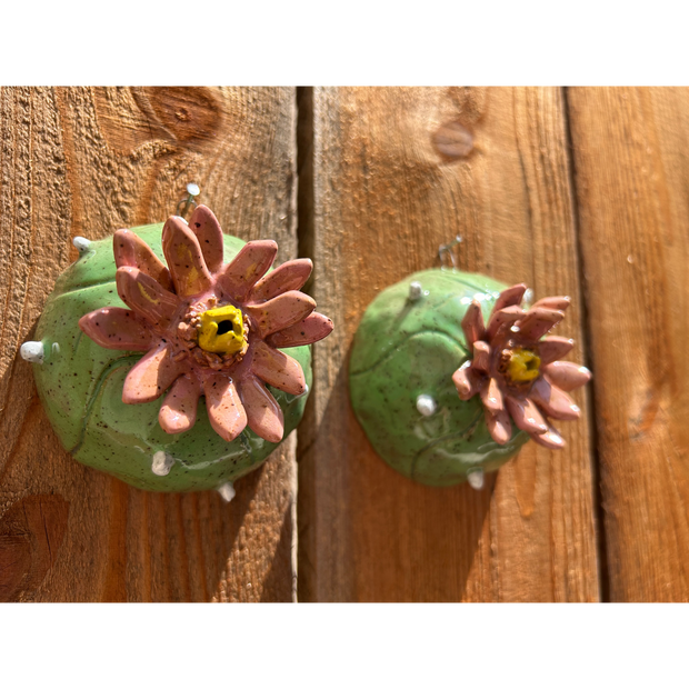 Ceramic sculpture of a pair of peyote cacti, with small white spikes and large blossomed pink flowers in the center.