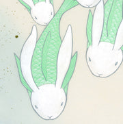 Paper circle with deckled edges and a soft blue and cream colored watercolor background. Blue and green fish with white bunny heads swim calmly. Close up showing bunny faces.