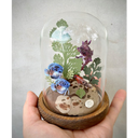 Mixed media sculpture of various colorful fish, made out of clay and swimming around cut paper leaves and plants. Fish are blue, red and purple. Scene is encased in a glass cloche.