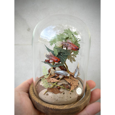 Mixed media sculpt red and silver fish swim around green cut paper plants and leaves. Scene is inside of glass cloche.