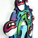 Painted flat wood sculpture of a blue skull with a circular wave of green and blue water coming out of its eye sockets. On the wave are several pink eyeballs. Close up side detailing.