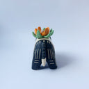 Matte surfaced ceramic sculpture of a black elephant with long white and gold tusks. Its body is patterned with cream colored lines, orange poppy flowers and It wears a fabric designed like mountains with a setting gold sun. Atop its back is an orange flower with green leaves.