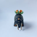 Matte surfaced ceramic sculpture of a black elephant with long white and gold tusks. Its body is patterned with cream colored lines, orange poppy flowers and It wears a fabric designed like mountains with a setting gold sun. Atop its back is an orange flower with green leaves.