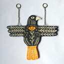 Flat ceramic artwork of a black bird with orange tail feathers, with both of its wings spread out horizontally. It has carved leaf patterns on its wings and body and an orange poppy flower on its chest.