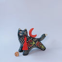 Ceramic figurine of a black wolf with white line detailing and red floral patterning. it holds a red tassel in its mouth and has a red crescent moon on its back.