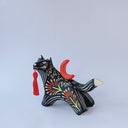 Ceramic figurine of a black wolf with white line detailing and red floral patterning. it holds a red tassel in its mouth and has a red crescent moon on its back.