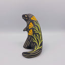 Matte finish ceramic sculpture of a T-Rex dinosaur, black with cream colored sgraffito line detailing and golden poppy flower designs on its back.