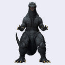 A detailed Godzilla action figure or collectible statue shown standing upright against a plain light gray background. The figure is predominantly dark textured gray with black shading, and small metallic gold accents are visible on the claws and mouth interior.