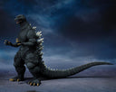 Godzilla action figure posed standing on a dark, smoky surface against a dramatic blue-black sky backdrop.