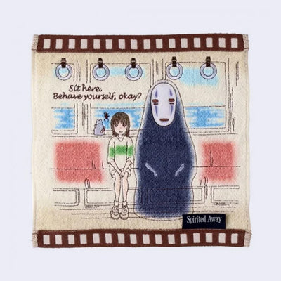Cream colored hand towel with brown square outline. Embroidered on is a scene from Spirited Away with the characters sitting on a train with text that reads, "Sit here. Behave yourself, okay?"